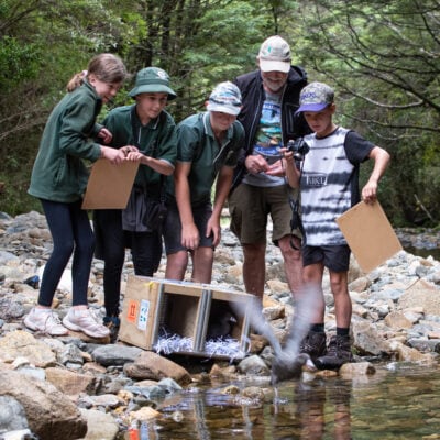 a group of people standing on rocks by a river with boxes
